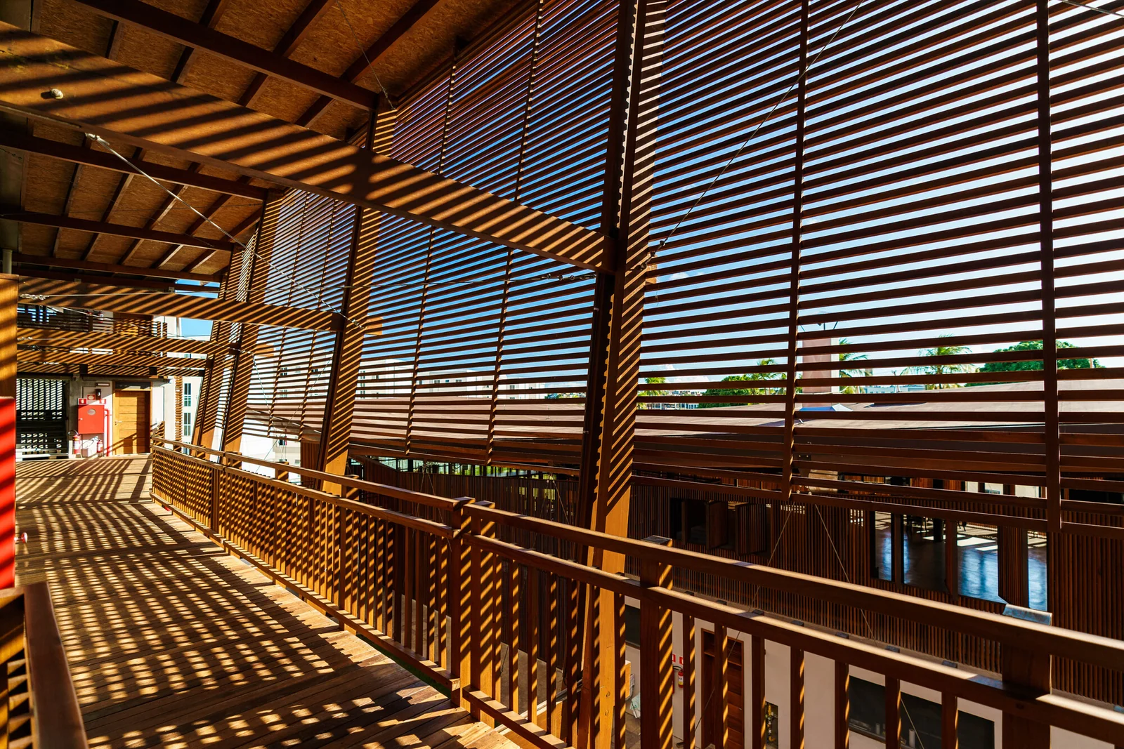 Galeria de circulação com proteção lateral, vigas e brises de madeira.